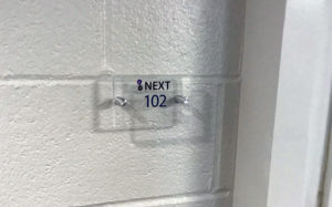 clear acrylic sign mounted with two silver standoffs that reads "NEXT 102"