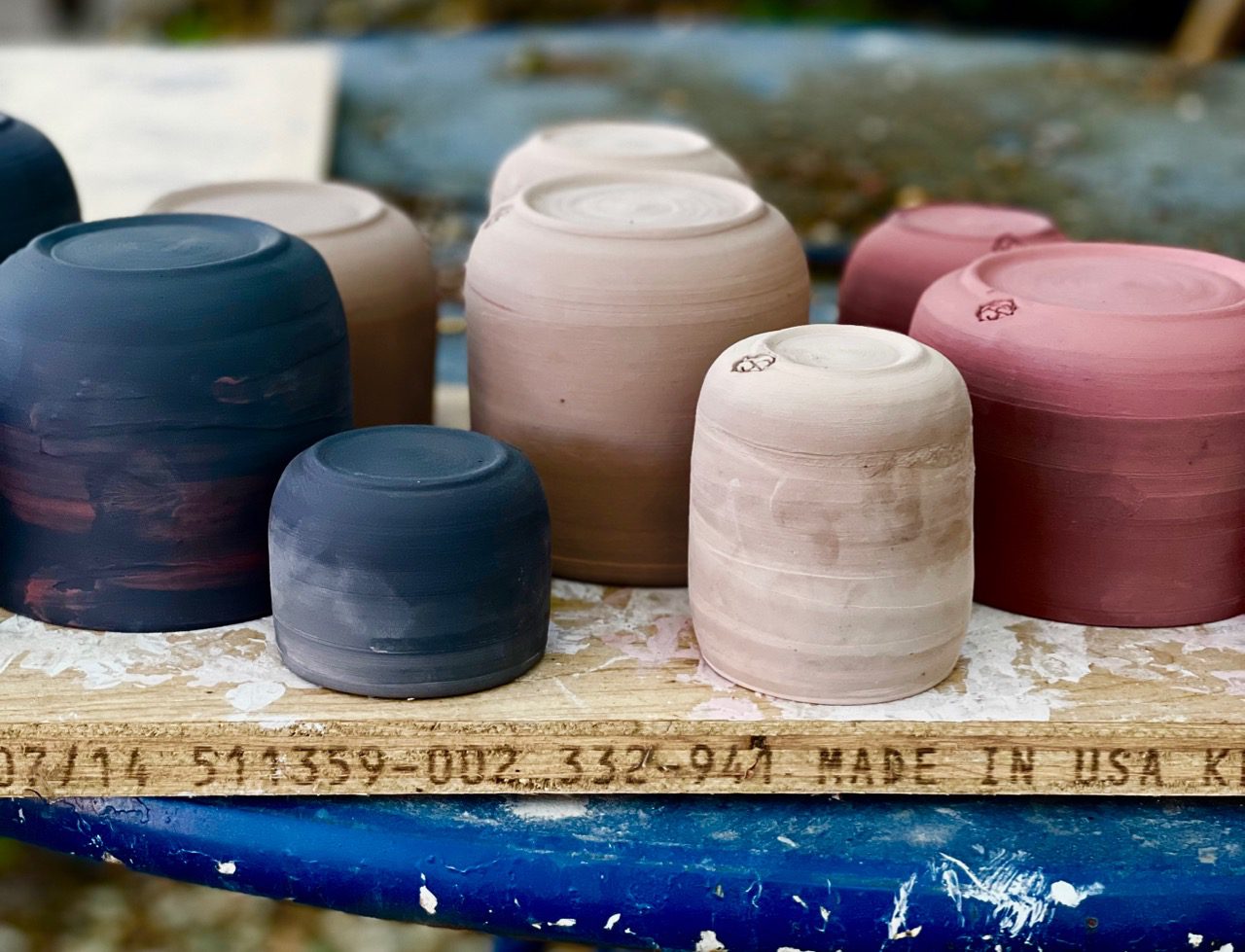 Black, pink, and red porcelain greenware pots upside down and butts-up on a wooden board