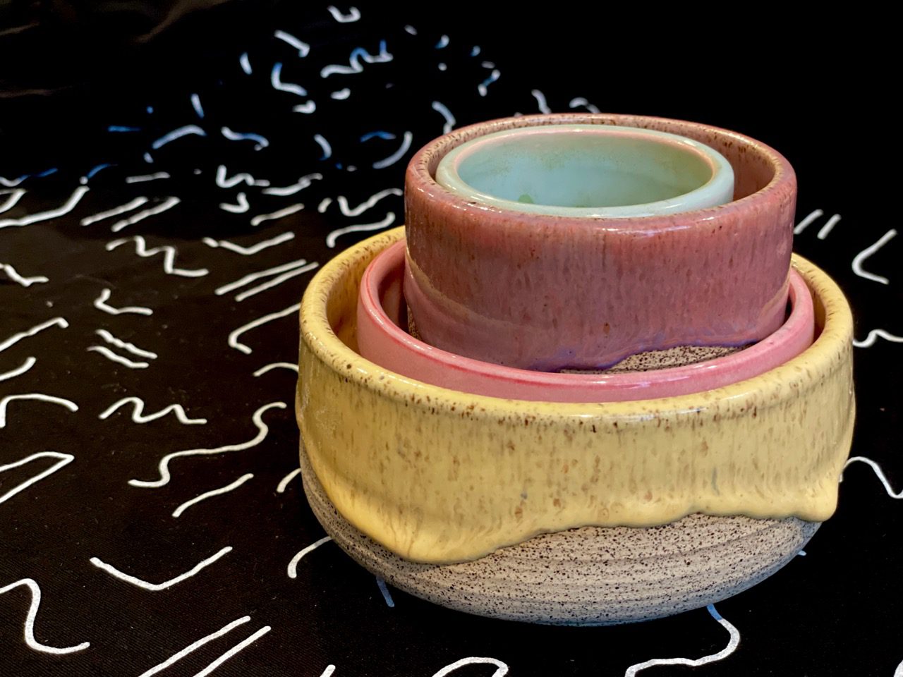 Colorful stack of ceramic bowls and cups with a black plus white squiggles fabric background