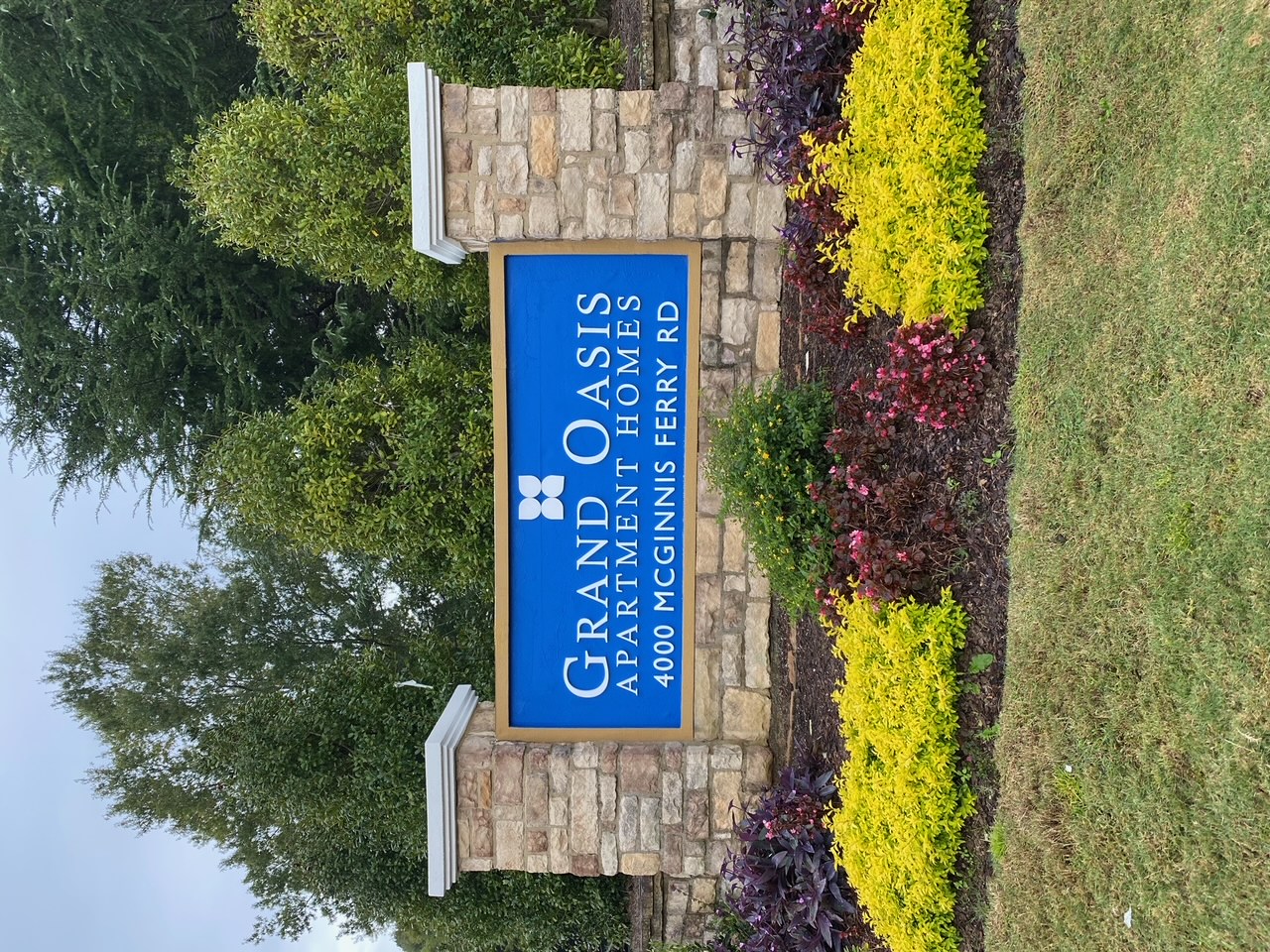 Grand Oasis Apartment Homes monument sign with stone pillars and blue panel at 4000 McGinnis Ferry Road — apartment community entrance signage.