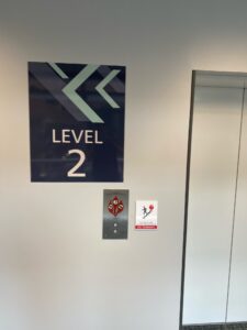 Parking garage wayfinding sign for Level 2 with arrow graphics, mounted beside elevator — directional building signage.