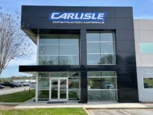 Blue “CARLISLE” channel letters with “Construction Materials” on a black panel entry tower with glass
