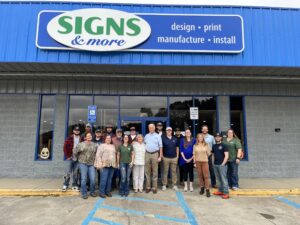 Signs & More team standing outside the Marietta, GA shop under the blue storefront sign